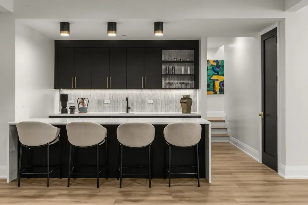 Lower-level bar with black cabinetry, open shelving and four upholstered stools