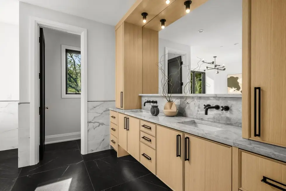 Bathroom with a long oak vanity, stone counter, black fixtures and marble wall tile