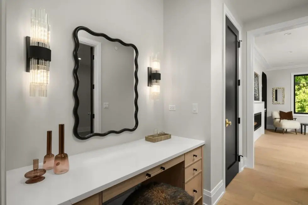 Oak makeup desk with a white top, a wavy black-framed mirror and fluted glass sconces