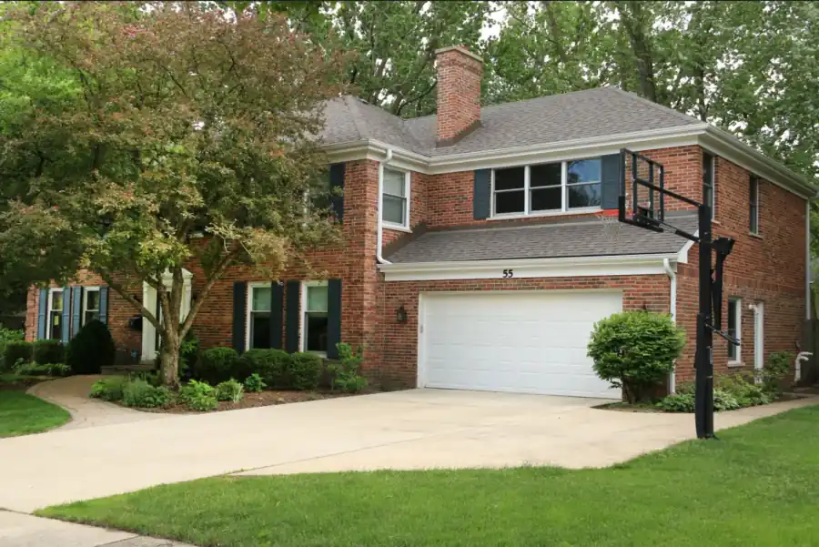 Red brick two-story home with a wide white garage door and a shingled roof