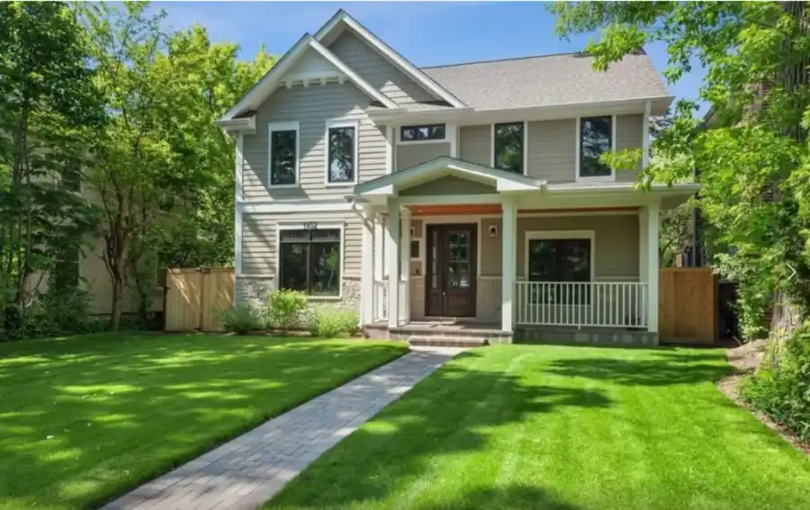 Grey lap-sided home with a columned front porch, white railing and a paver walk