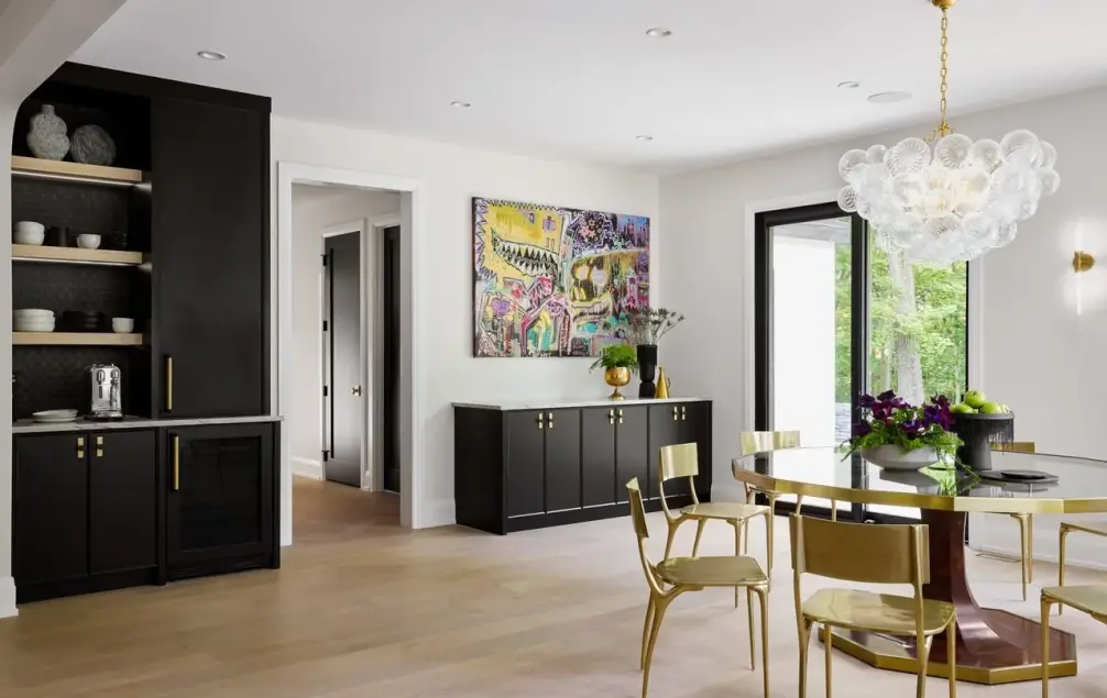Black cabinet wall with open oak shelves and a coffee station beside a round dining table with brass-framed chairs