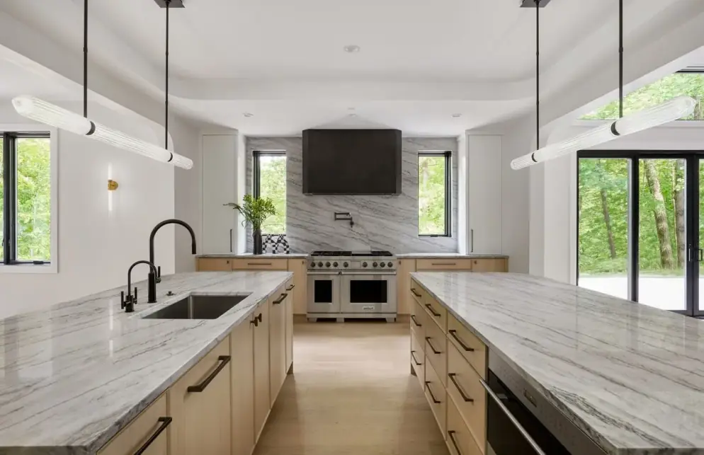Veined stone slab backsplash behind a dual-oven range with a black hood, oak cabinets and stone countertops